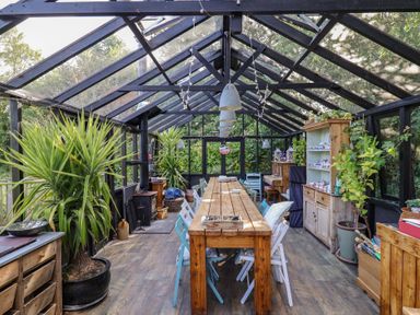 A conservatory with a long table and plants at The Old Dairy in Colyton