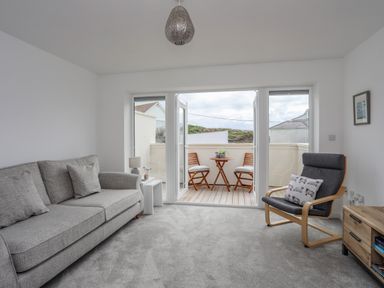 A sitting room with grey sofa and armchair opening onto a small balcony with wooden table and chairs at 9 Lon Y Dryw in Trearddur Bay