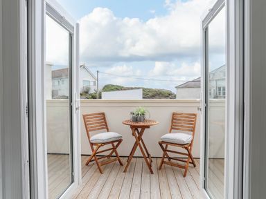 A balcony with two wooden chairs and a round wooden table with plants at 9 Lon Y Dryw in Trearddur Bay