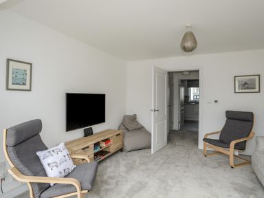 A living room with two gray armchairs a bean bag a wooden TV stand and a wall-mounted TV at 9 Lon Y Dryw in Trearddur Bay