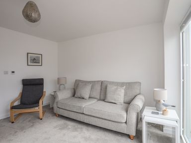 A living room with a gray sofa two side tables with lamps a wooden framed armchair and a framed picture on the wall at 9 Lon Y Dryw in Trearddur Bay