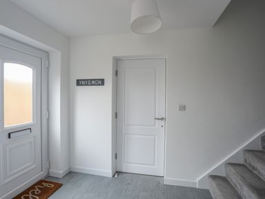 An entrance hallway with a white door and stairs with grey carpet at 9 Lon Y Dryw in Trearddur Bay