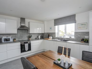 A kitchen with white cabinets a stove microwave sink and a wooden dining table at 9 Lon Y Dryw in Trearddur Bay