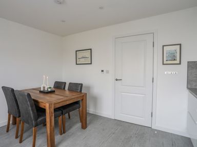A dining area with a wooden table and four chairs near a white door and two framed pictures at 9 Lon Y Dryw Trearddur Bay