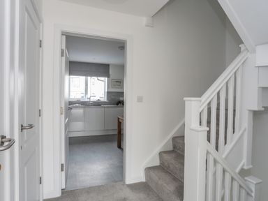 A hallway with carpeted stairs and a view into a kitchen with a window at 9 Lon Y Dryw in Trearddur Bay
