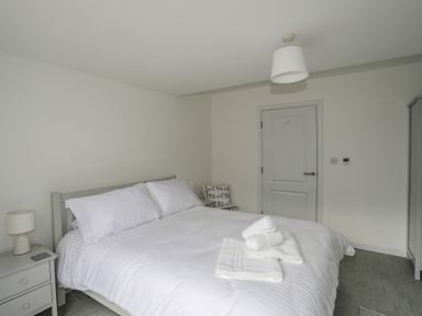 A bedroom with a double bed white bedding nightstand with lamp and folded towels on the bed at 9 Lon Y Dryw in Trearddur Bay