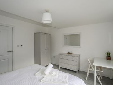 A bedroom with a bed, wardrobe, dresser with mirror, table with chair, and a plant at 9 Lon Y Dryw in Trearddur Bay