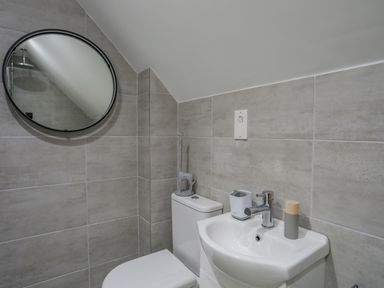 A bathroom with a toilet sink and round mirror at 9 Lon Y Dryw in Trearddur Bay