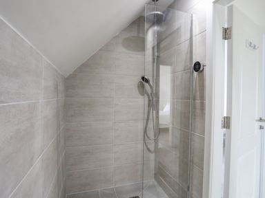 A walk-in shower with glass door and gray tiles at 9 Lon Y Dryw in Trearddur Bay