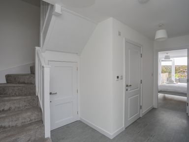 A hallway with gray carpeted stairs white doors and a view into a bedroom at 9 Lon Y Dryw in Trearddur Bay