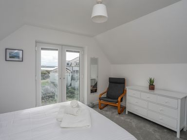 A bedroom with a bed, a black chair, a white dresser, a mirror, and a small plant at 9 Lon Y Dryw in Trearddur Bay