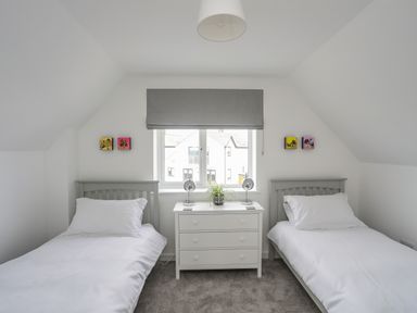 A bedroom with two single beds a white dresser and a window with a gray blind at 9 Lon Y Dryw in Trearddur Bay
