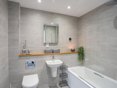 A bathroom with a toilet sink bathtub and shelf with decorative items at 9 Lon Y Dryw in Trearddur Bay