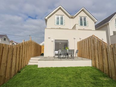 A backyard with a patio table and chairs and grass enclosed by wooden fences at 9 Lon Y Dryw in Trearddur Bay