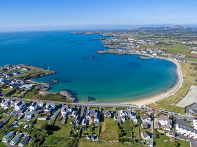 A coastal village with houses along a curved beach and blue sea at 9 Lon Y Dryw in Trearddur Bay