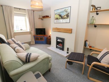 A sitting room with a green sofa and armchair around a fireplace and a corner TV unit at Llety Bach in Caernarfon
