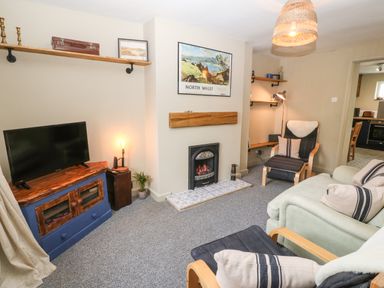A living room with a TV on a wooden cabinet a fireplace and seating at Llety Bach in Caernarfon