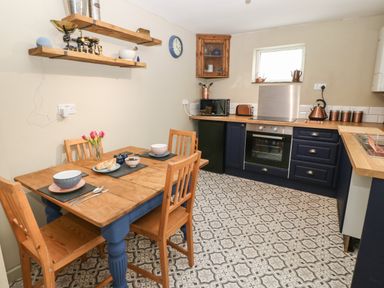 A kitchen with a wooden dining table and chairs a stove microwave and sink at Llety Bach in Caernarfon