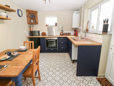A kitchen with wooden countertops blue cabinets patterned floor and a wooden dining table at Llety Bach in Caernarfon