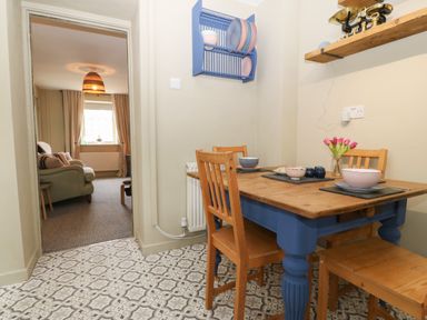 A dining area with wooden table and chairs and dish rack on wall with a living room visible through the doorway at Llety Bach in Caernarfon