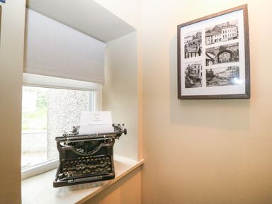 A typewriter on a window sill next to a framed collage of black and white photos on a wall at Llety Bach in Caernarfon