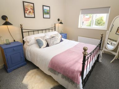 A bedroom with a metal bed frame with white bedding and pink throw at Llety Bach in Caernarfon