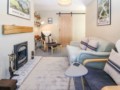 A sitting room with armchairs a sofa a fireplace and a wooden sliding door at Llety Bach in Caernarfon