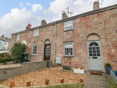 An outdoor view of stone cottages with doors windows flower pots and gravel gardens at Llety Bach in Caernarfon