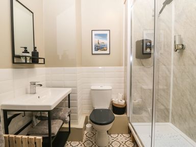 A bathroom with a sink and mirror on the left a toilet in the center and a shower enclosure on the right at Llety Bach in Caernarfon