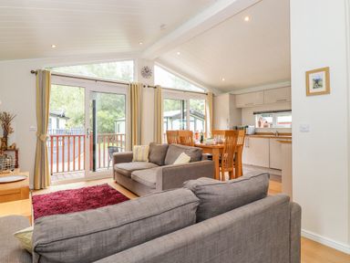 An open living and dining area with gray sofas a red rug a wooden dining table and a kitchen with white cabinets at Garuda Calgarth 19 White Cross Bay near Windermere
