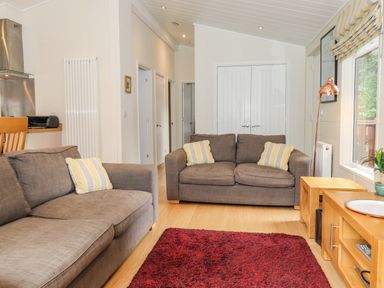 A living room with two grey sofas yellow striped cushions a red rug and wooden furniture at Garuda Calgarth 19 White Cross Bay near Windermere
