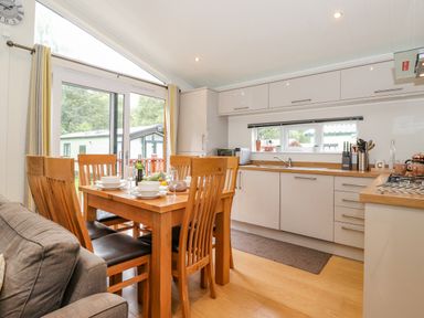 A dining area with a wooden table and chairs next to a kitchen with white cabinets and a window at Garuda Calgarth 19 White Cross Bay near Windermere