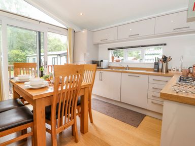 A kitchen with wooden dining table set with plates and bowls next to white cabinets and a window at Garuda Calgarth 19 White Cross Bay near Windermere