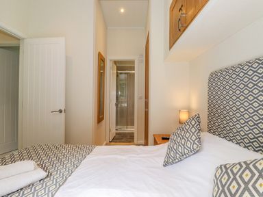 A bedroom with a bed featuring patterned headboard and pillows a bedside table with lamp and a hallway leading to a bathroom shower at Garuda Calgarth 19 White Cross Bay near Windermere