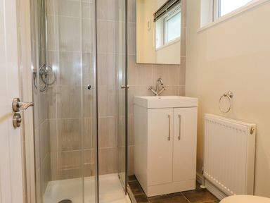A bathroom with a shower enclosure a sink with cabinet a radiator and a window at Garuda Calgarth 19 White Cross Bay near Windermere