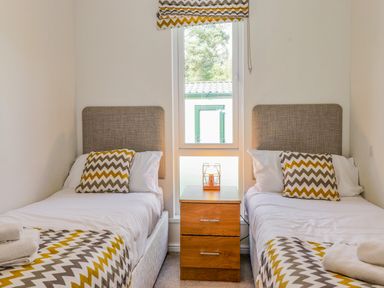 A bedroom with two single beds with chevron patterned pillows and blankets and a wooden nightstand between at Garuda Calgarth 19 White Cross Bay near Windermere