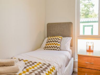 A bedroom with a single bed a chevron patterned pillow folded towels on the bed and a wooden bedside table with a candle holder at Garuda Calgarth 19 White Cross Bay near Windermere