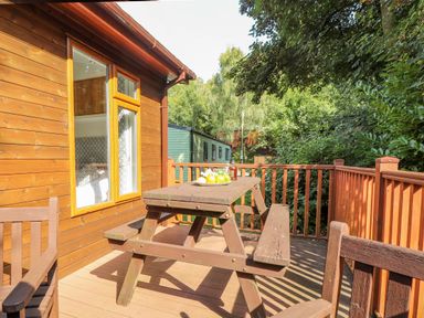 A wooden deck with a picnic table and benches next to a cabin with a window showing a bed at Garuda Calgarth 19 White Cross Bay near Windermere
