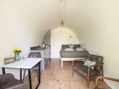 A small curved room with a bed at the end a kitchenette on the left and a table with chairs and armchairs at Tyddyn Parthle Pod 1 in Bontnewydd Gwynedd