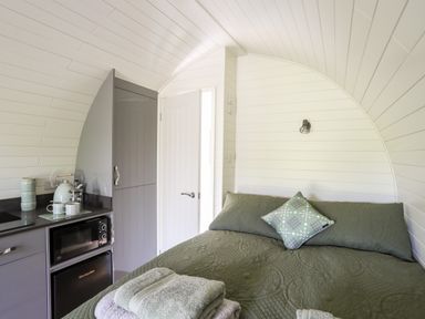 A small room with a bed covered with green bedding next to a kitchenette with a microwave and a fridge at Tyddyn Parthle Pod 1 in Bontnewydd Gwynedd