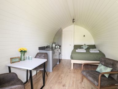 A small room with a bed green pillows a kitchenette a table with chairs and a vase of flowers at Tyddyn Parthle Pod 1 in Bontnewydd Gwynedd
