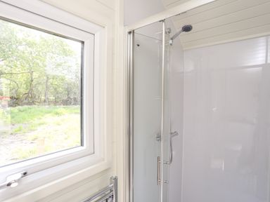 A bathroom with a glass shower enclosure and a window showing trees outside at Tyddyn Parthle Pod 1 in Bontnewydd Gwynedd