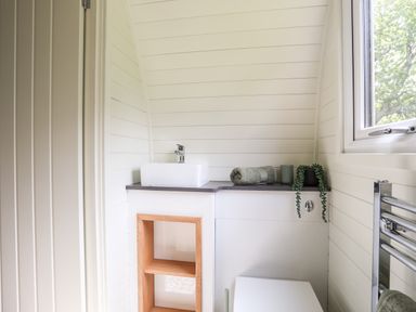 A bathroom with a white sink on a countertop a rolled towel a green plant a towel rack and a window at Tyddyn Parthle Pod 1 in Bontnewydd Gwynedd