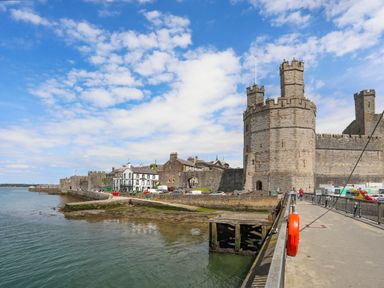 A coastal scene with a stone castle wall and tower near the water and a walkway alongside at Tyddyn Parthle Pod 1 in Bontnewydd Gwynedd