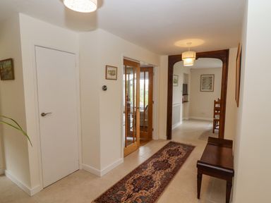 A hallway with a patterned runner rug a wooden bench wooden framed glass doors and framed pictures on cream walls at The Gables in Sheepscombe