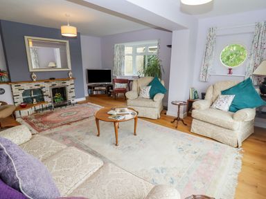 A living room with armchairs a coffee table a fireplace and a television at The Gables in Sheepscombe