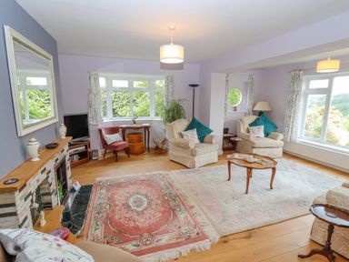 A living room with armchairs rugs coffee table and windows showing greenery at The Gables in Sheepscombe