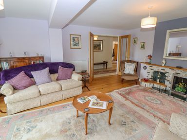 A living room with a beige sofa with pillows a wooden coffee table a fireplace and a brown armchair at The Gables in Sheepscombe