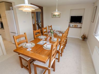 A dining room with a wooden table and chairs set with plates glasses and a bottle at The Gables in Sheepscombe
