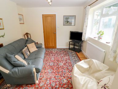 A living room with a sofa bean bag television and a red patterned rug at The Gables in Sheepscombe